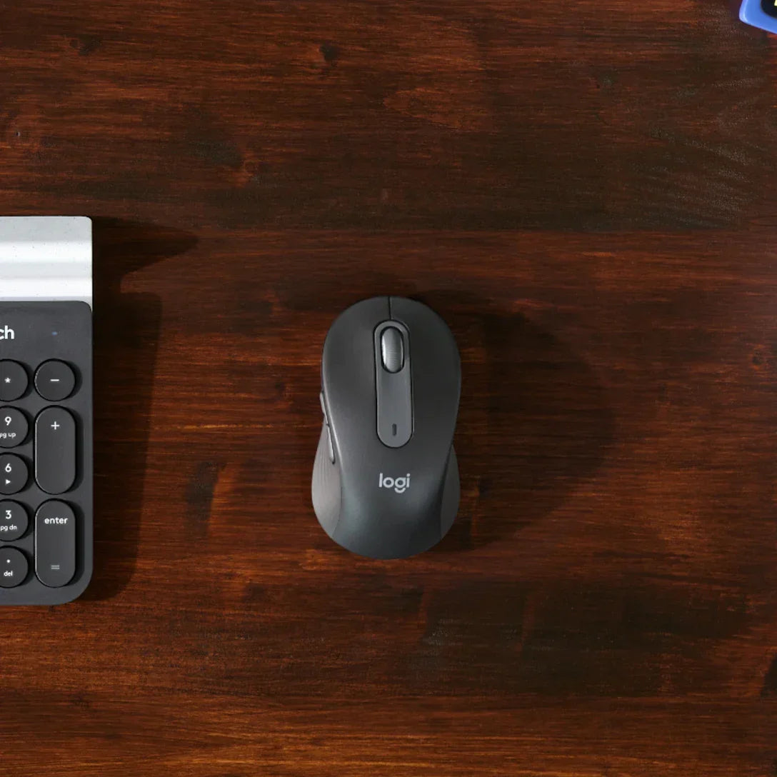 Logitech M650 mouse ahşap masa üzerinde üstten görünüm, yanında klavye detaylı